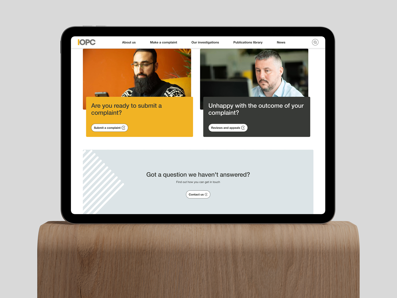 Tablet on a wooden stand showing IOPC website with options to submit a complaint, request reviews, and contact support.